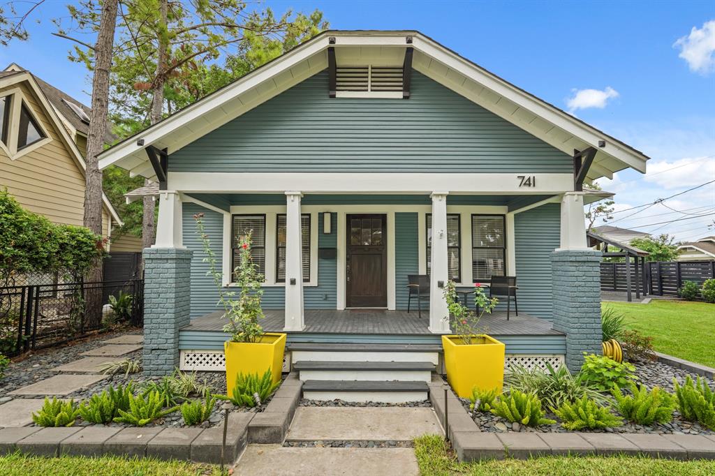 A charming Craftsman home located in the Heights, featuring a cozy front porch perfect for relaxing on a warm afternoon. The house boasts classic architectural details, including tapered columns and a wide overhanging roof, creating a welcoming and timeless appeal. The front yard is beautifully landscaped, adding to the home’s inviting atmosphere