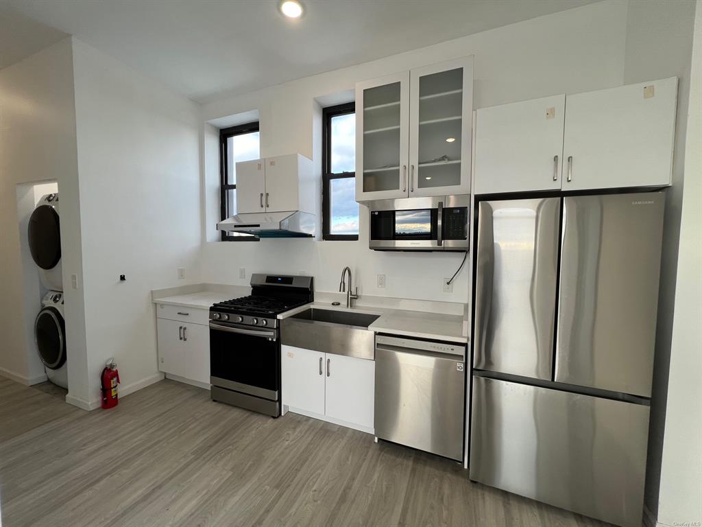 Kitchen with stacked washing maching and dryer, light wood-type flooring, white cabinetry, and appliances with stainless steel finishes