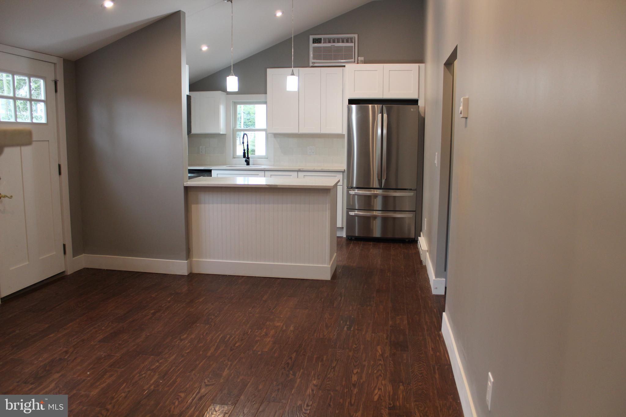 an empty room with wooden floor and kitchen view