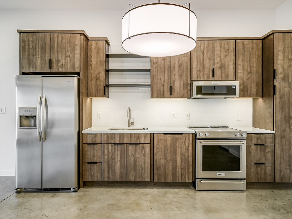 This modern kitchen blends sleek functionality with natural elements. Washed wood-like cabinets create a warm, rustic touch, contrasting beautifully with stainless steel appliances for a contemporary vibe.