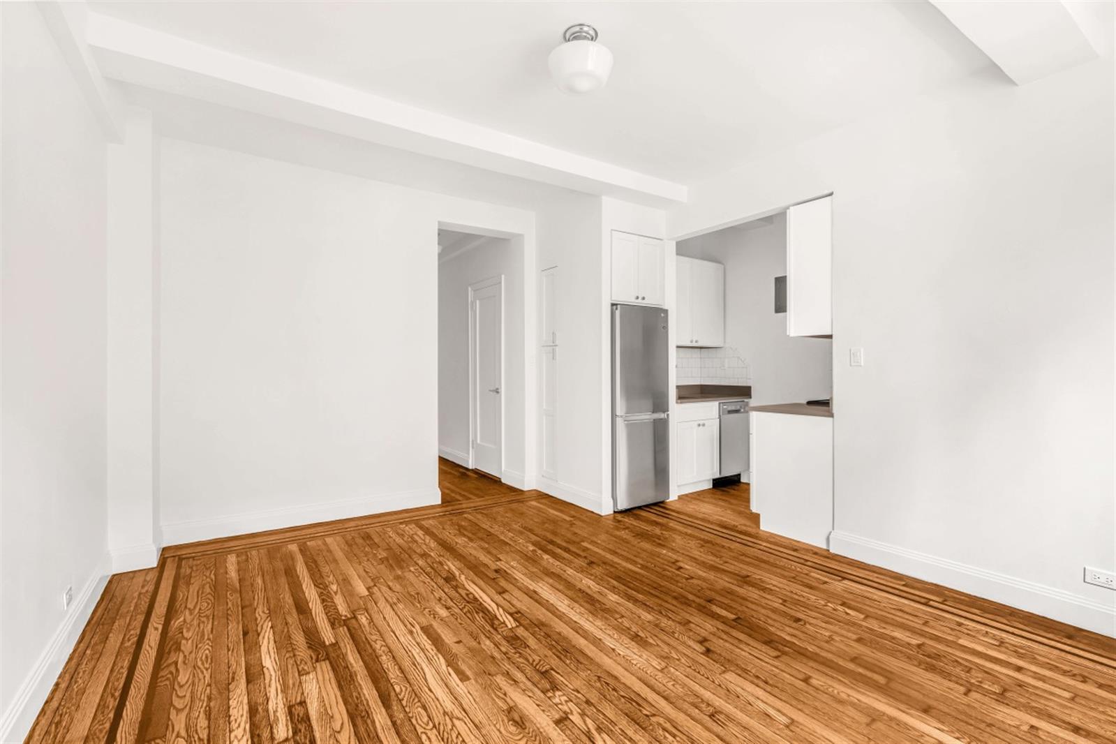 a view of kitchen and empty room with wooden floor