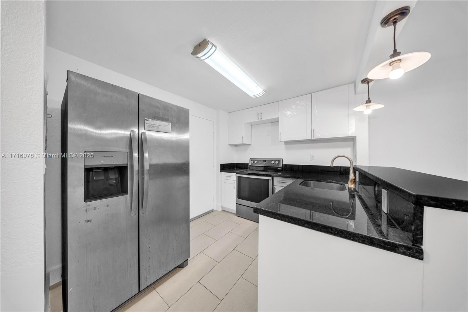 a kitchen with granite countertop a refrigerator a sink and white cabinets