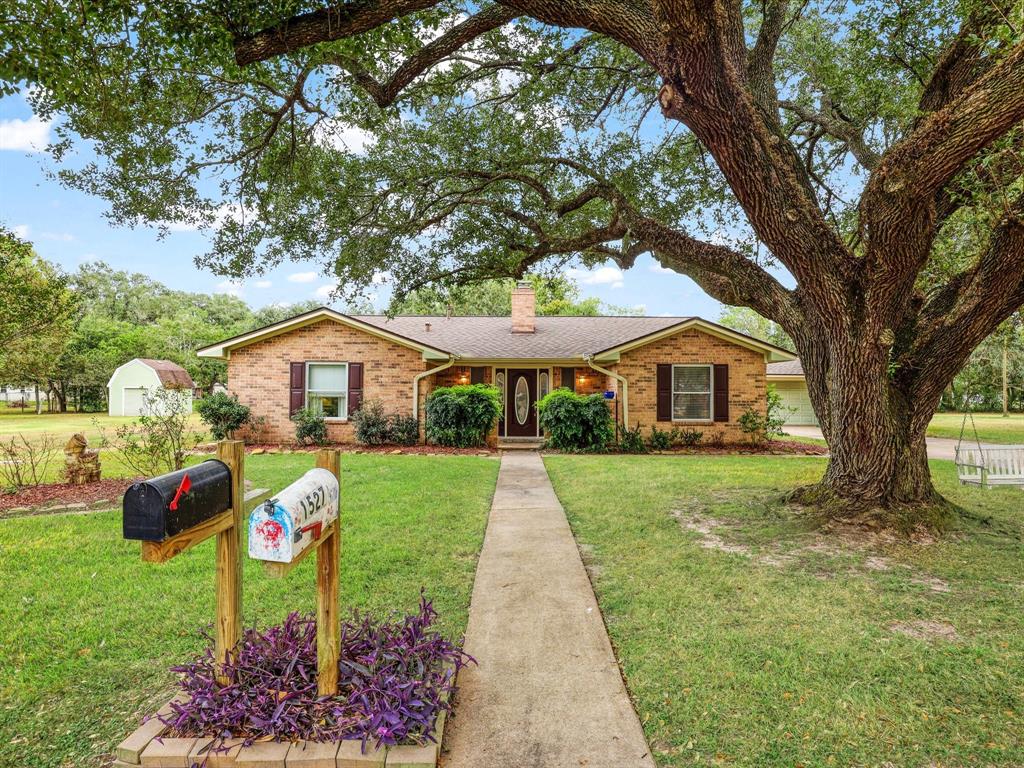 Charming single-story brick home nestled under a majestic oak tree, featuring a welcoming entrance, a classic design, and a spacious front yard with a traditional mailbox.