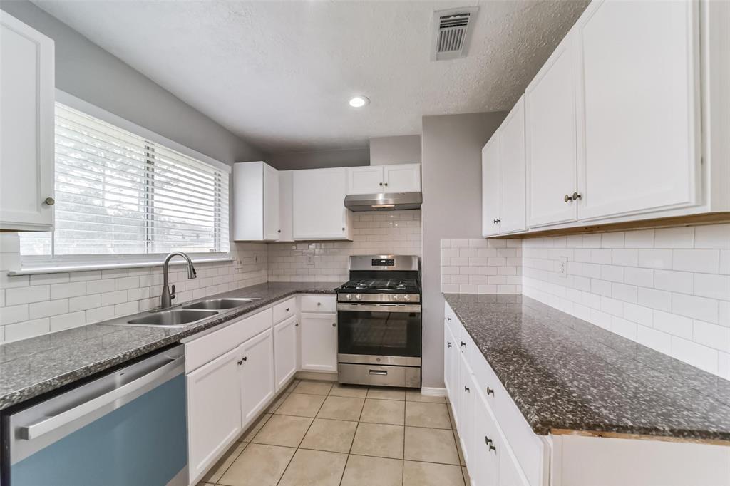 a kitchen with granite countertop white cabinets stainless steel appliances a sink and a window