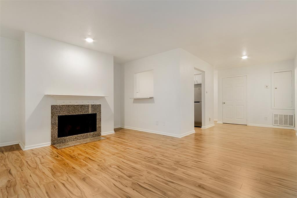 a view of an empty room with wooden floor fireplace and a window