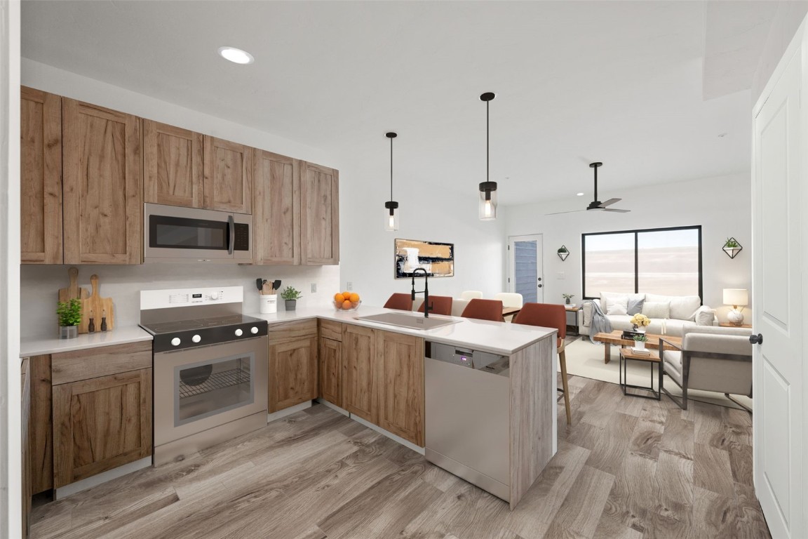 Kitchen featuring kitchen peninsula, appliances with stainless steel finishes, light wood-type flooring, sink, and pendant lighting