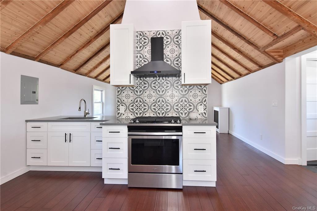 Kitchen with wall chimney range hood, white cabinets, and stainless steel stove