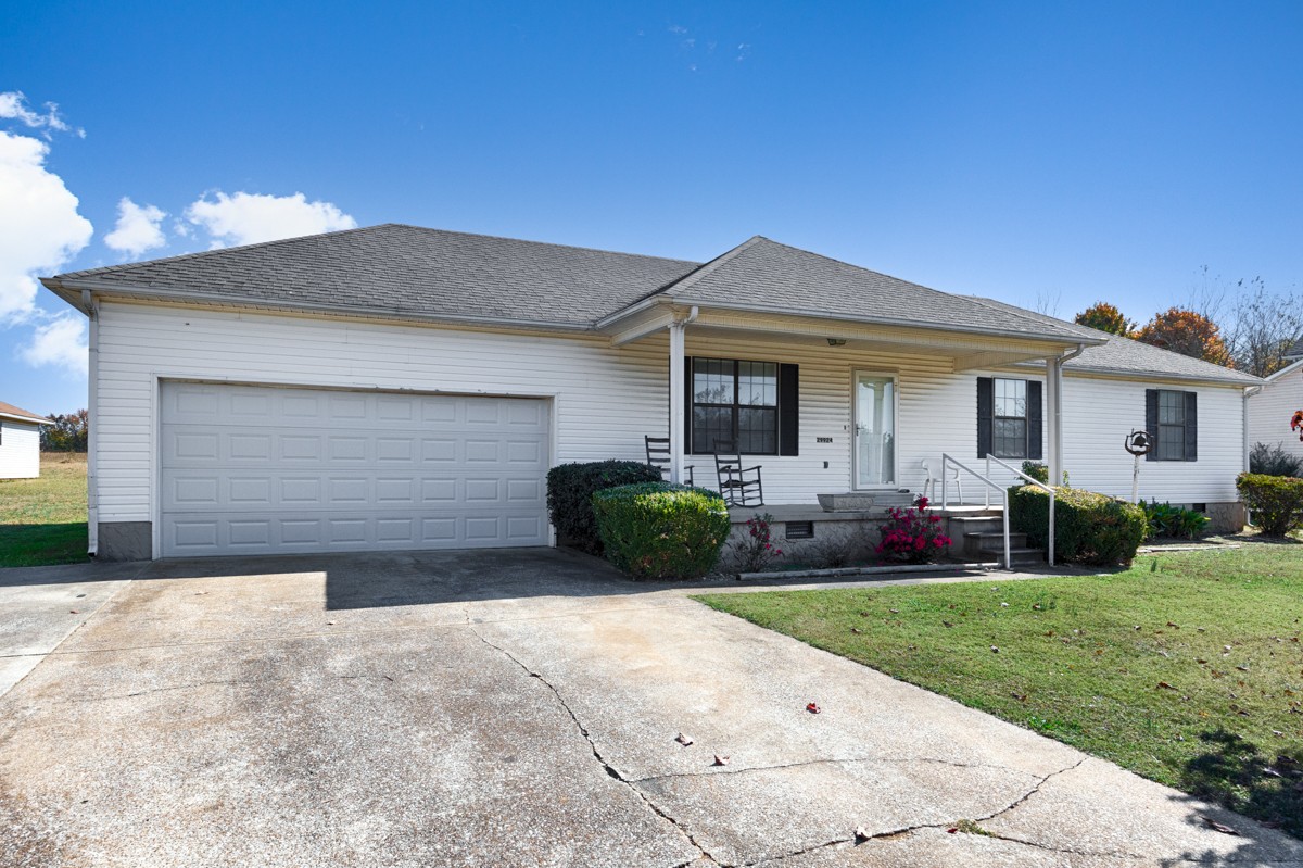 Front of house- 2-car attached garage with single rollup door, concrete driveway and sidewalk, covered front porch, simple landscaping