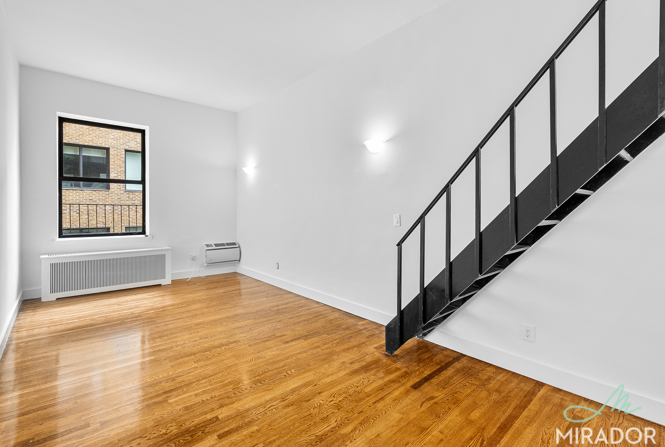 a view of an empty room with wooden floor and stairs