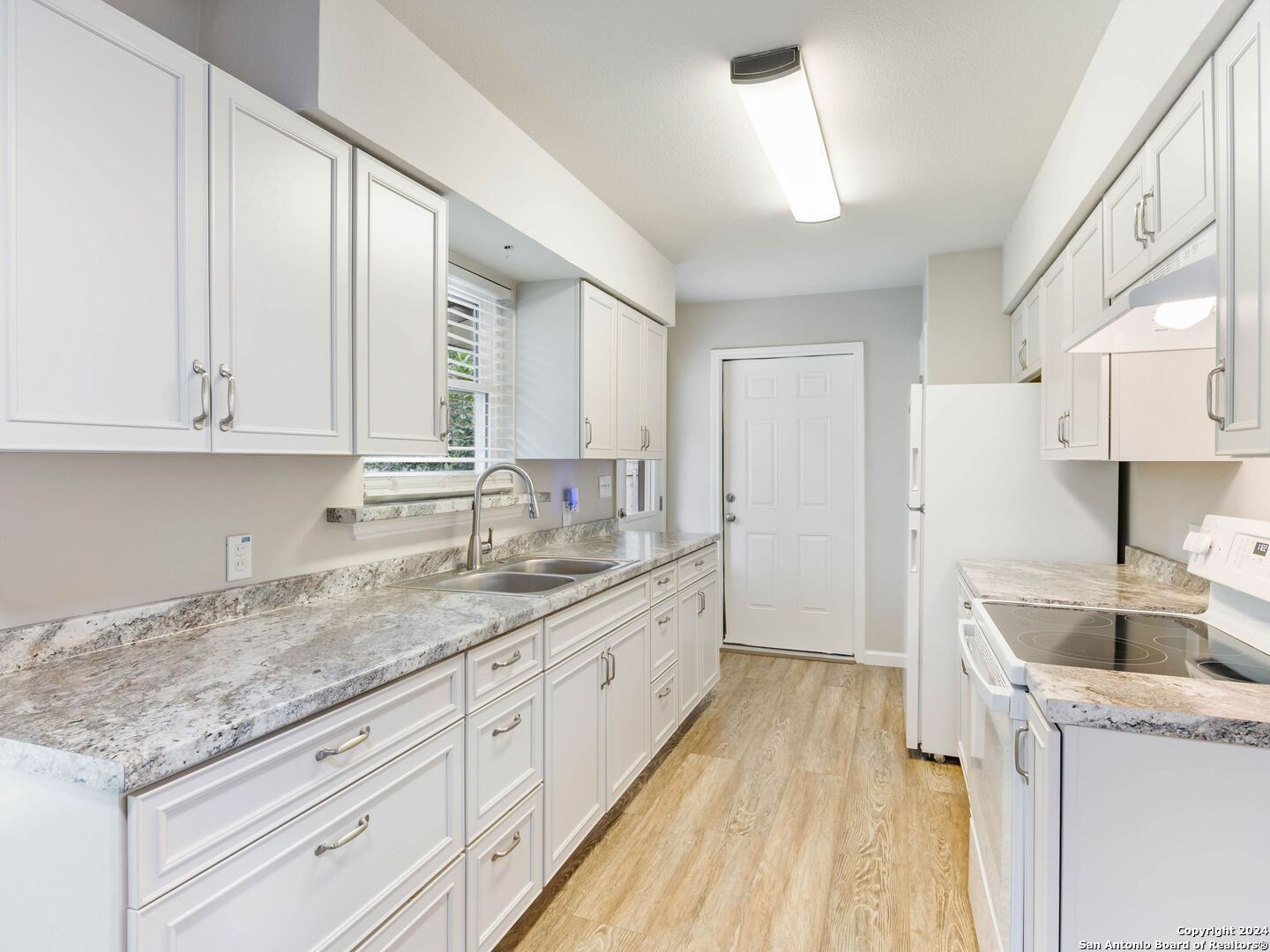 a kitchen with a sink dishwasher a stove and white cabinets with wooden floor