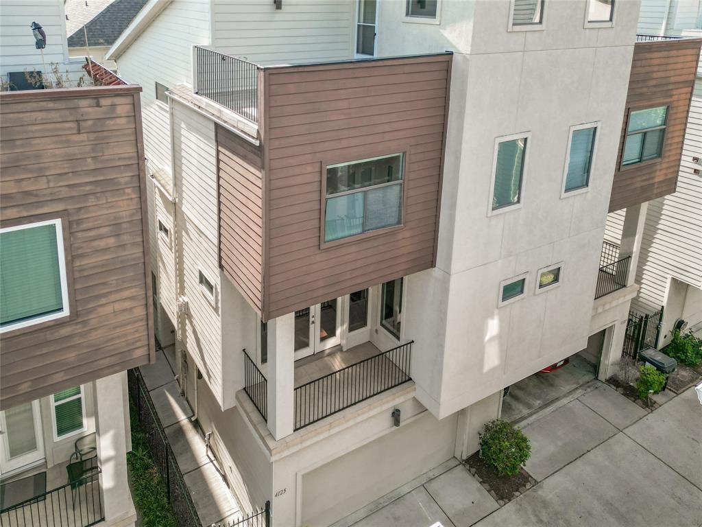 Modern multi-story home with a contemporary exterior featuring a mix of wood and stucco finishes. It includes a small balcony and an attached garage, set in a compact neighborhood layout.