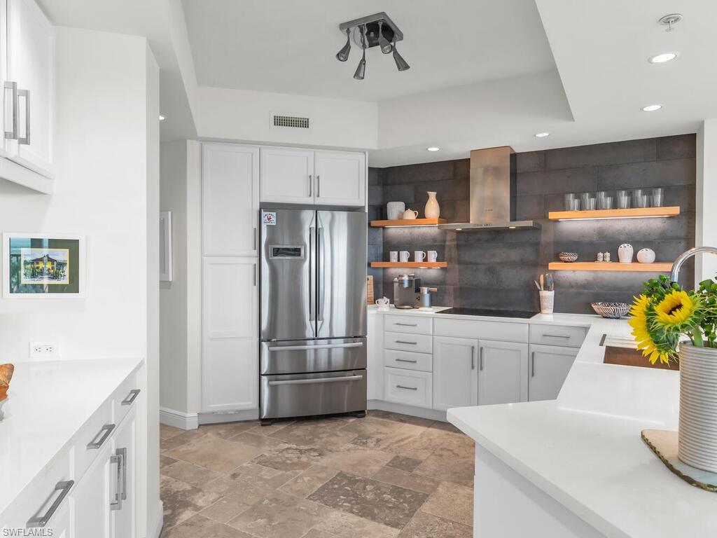 Kitchen with wall chimney exhaust hood, stainless steel fridge, white cabinetry, and light tile floors