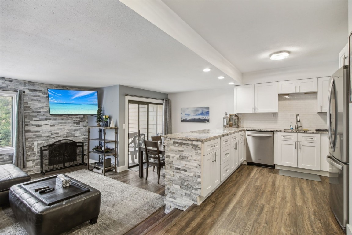 Kitchen featuring stainless steel appliances, a fireplace, kitchen peninsula, dark hardwood / wood-style floors, and white cabinetry