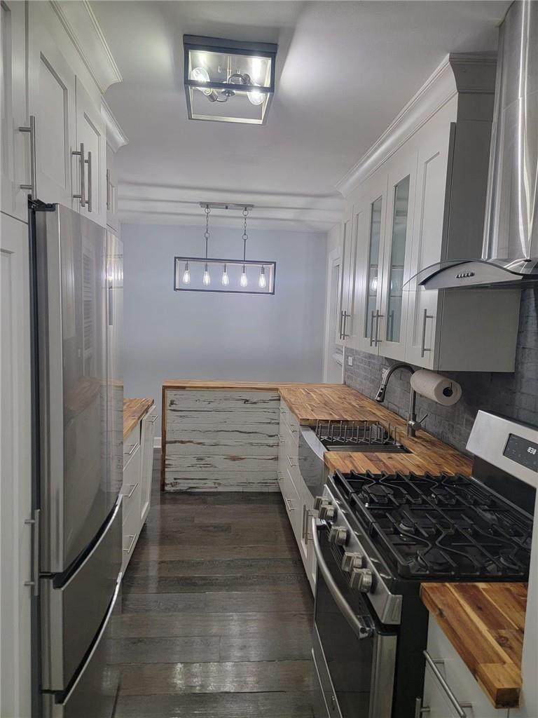 Kitchen featuring appliances with stainless steel finishes, white cabinetry, wood counters, and wall chimney range hood