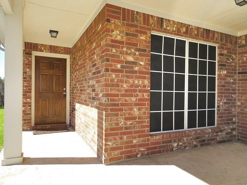 This is a home's covered entryway featuring a large wooden front door and a spacious window with dark frames, all set against a classic red brick exterior.