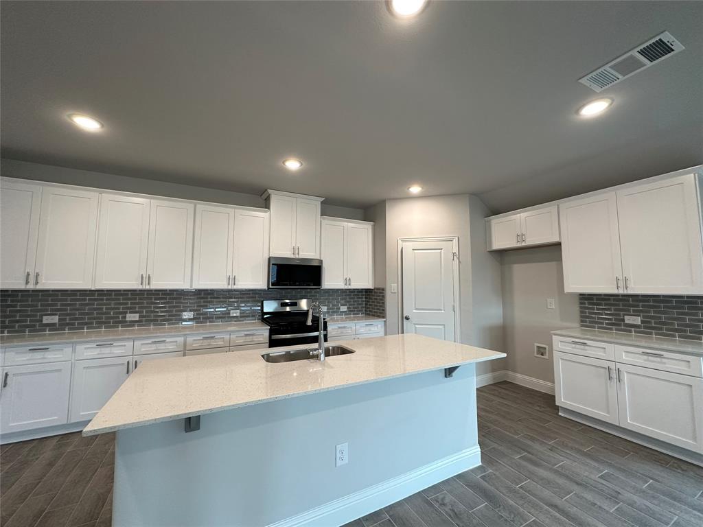 Kitchen with white cabinets, dark hardwood / wood-style flooring, stainless steel appliances, and a kitchen island with sink