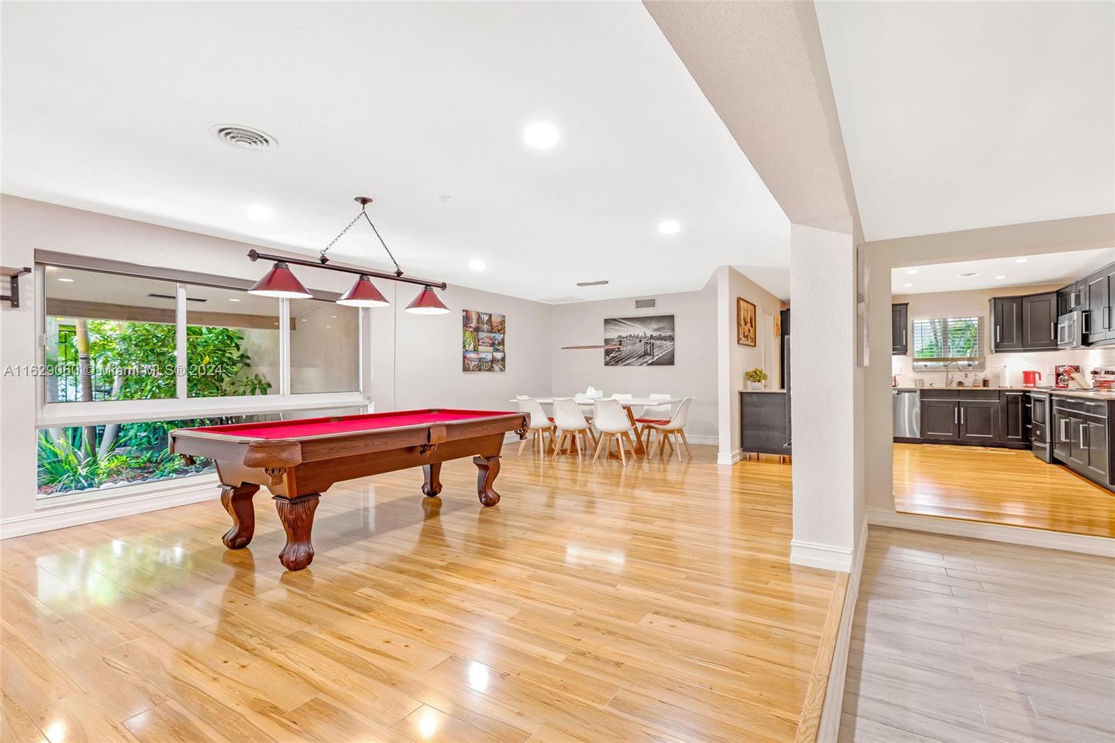 a room with wooden floors pool table and windows