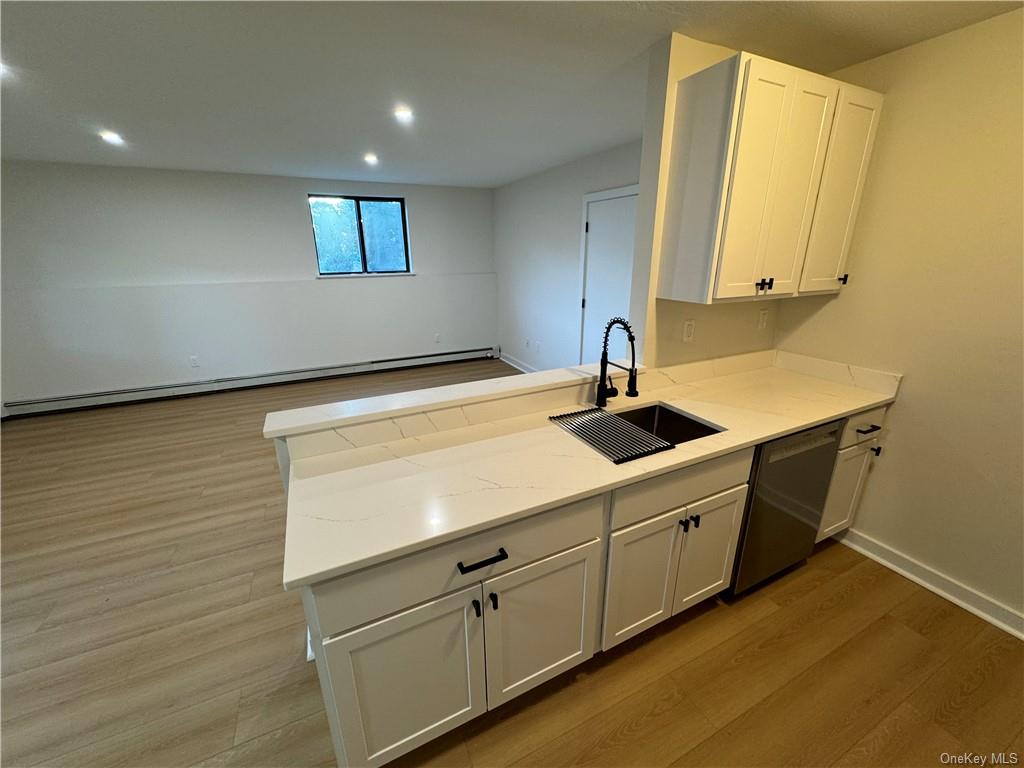 Kitchen with stainless steel dishwasher, white cabinets, sink, and light wood-type flooring