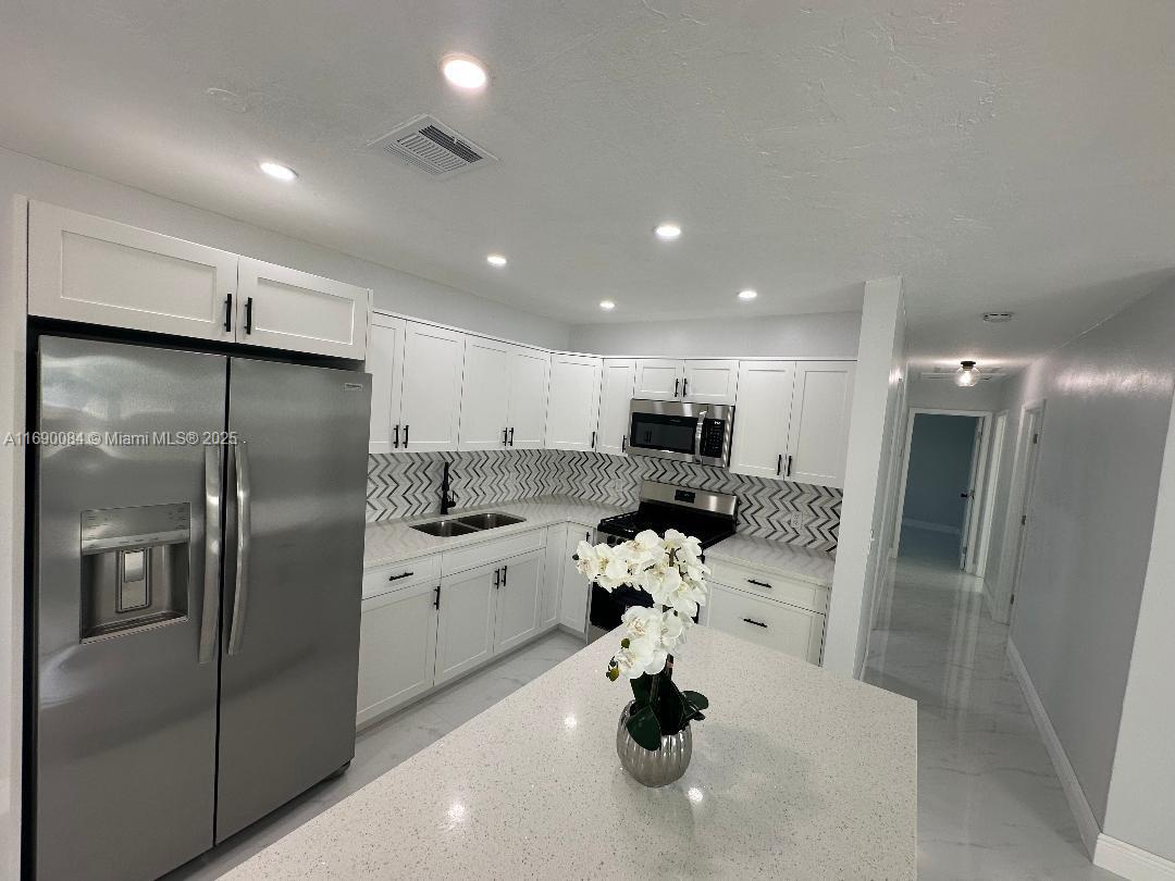 a kitchen with stainless steel appliances kitchen island granite countertop a refrigerator and a sink