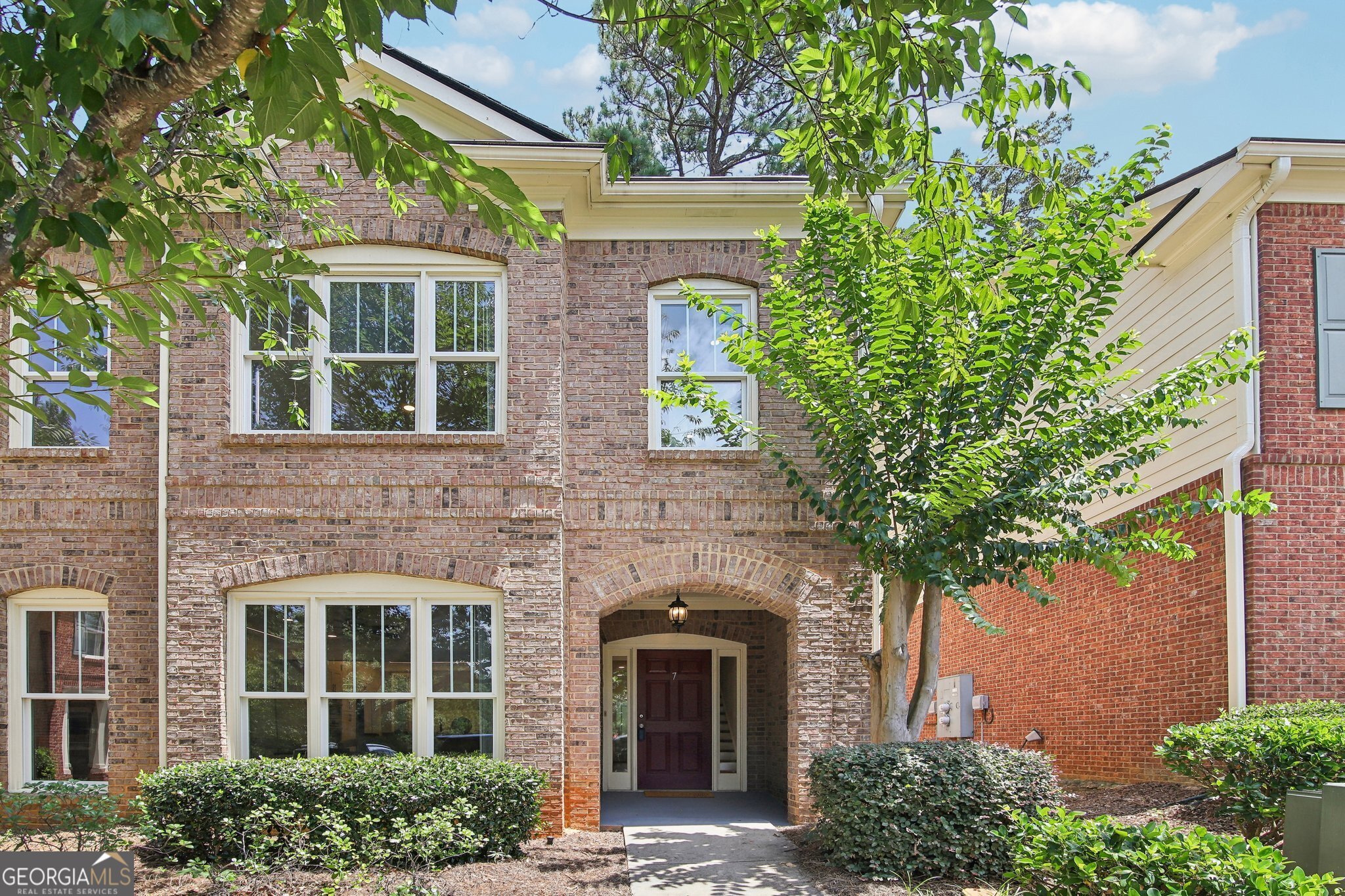 front view of a brick house with a large window and potted plants