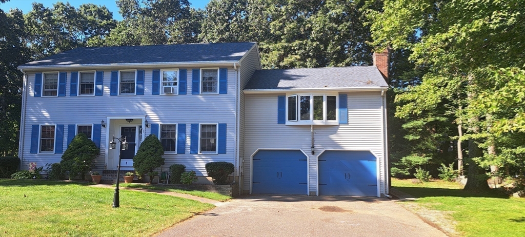 a view of a brick house with a yard plants and a large tree