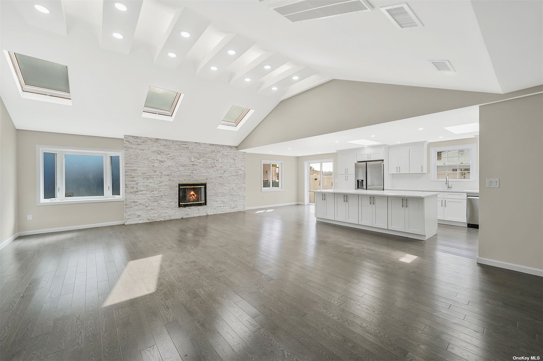 a view of an empty room with wooden floor and a kitchen