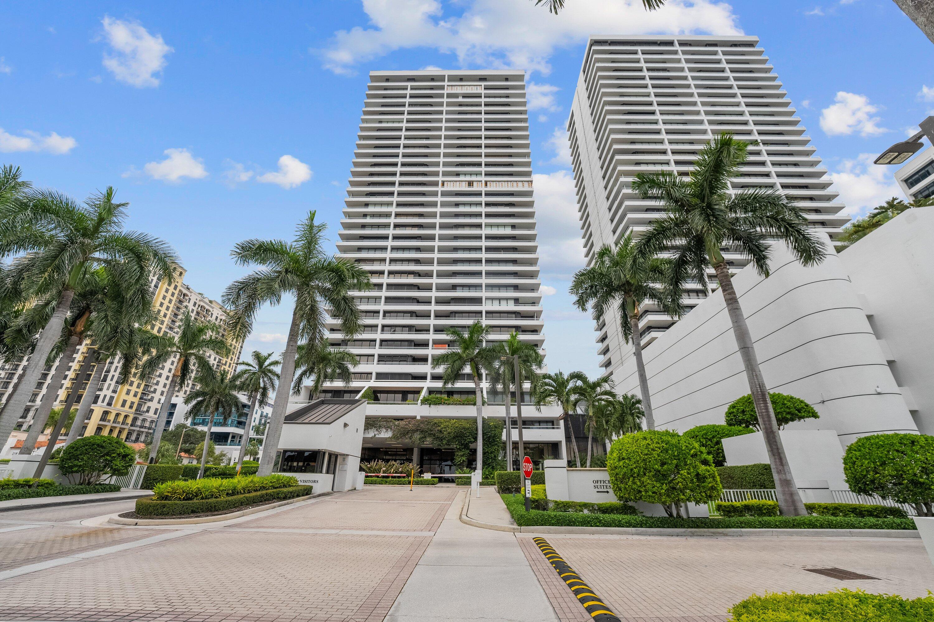 a front view of a residential apartment building with a yard and palm trees