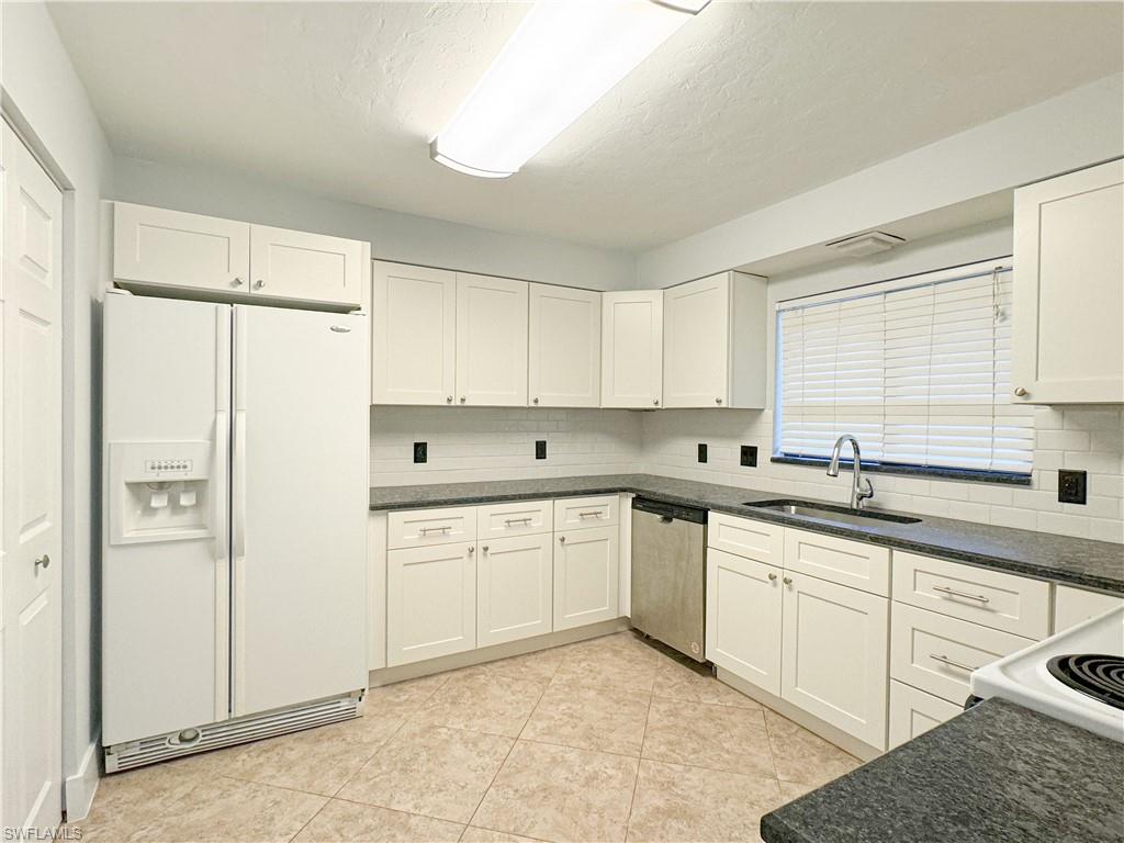 Kitchen with sink, stainless steel dishwasher, white cabinetry, white fridge with ice dispenser, and decorative backsplash