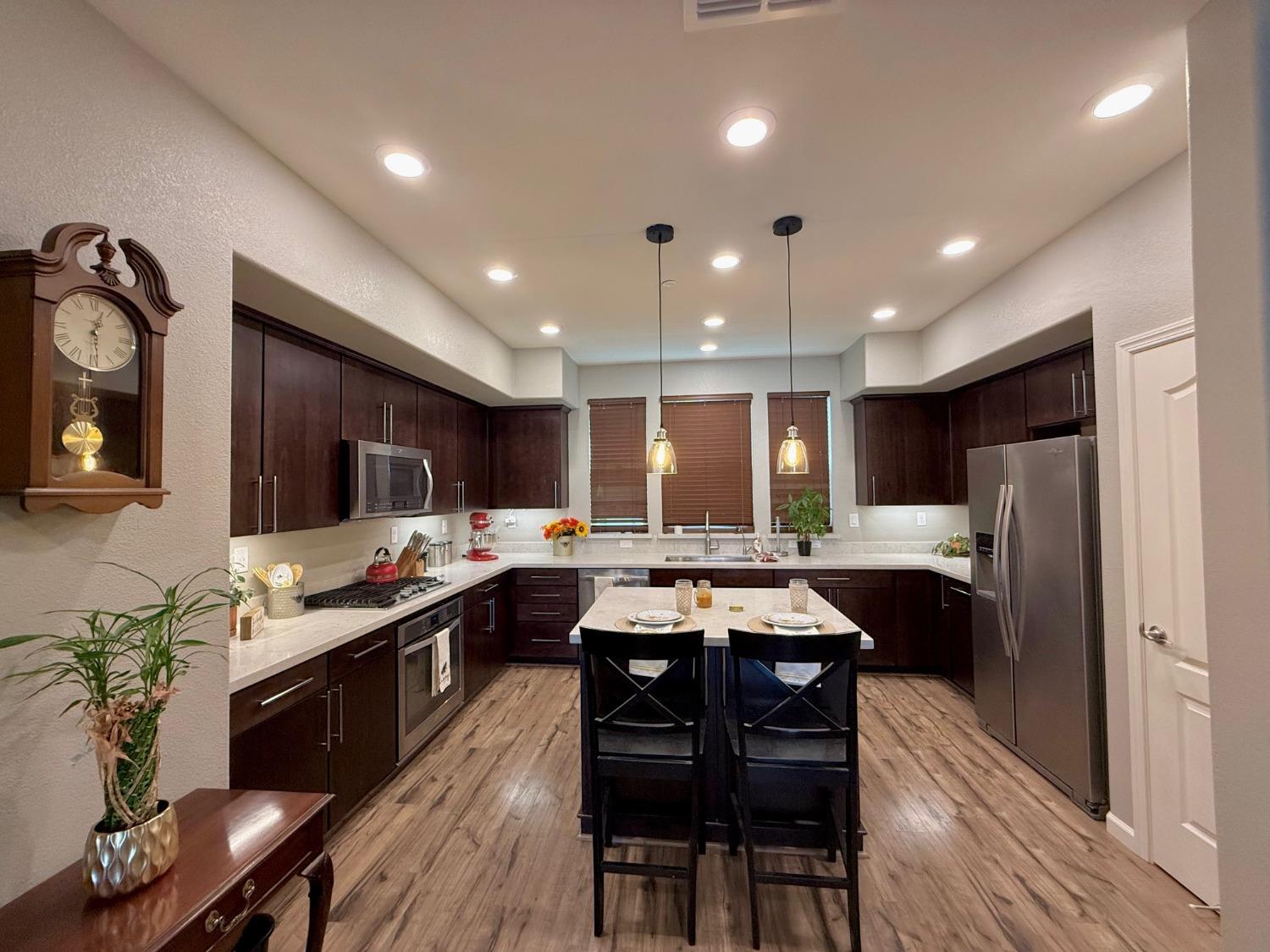 a kitchen with stainless steel appliances kitchen island granite countertop a stove a refrigerator a sink a dining table and chairs with wooden floor