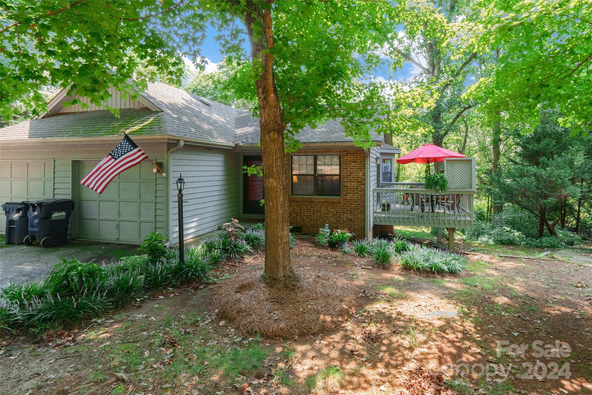 a view of a small house in front of a yard with plants and large trees