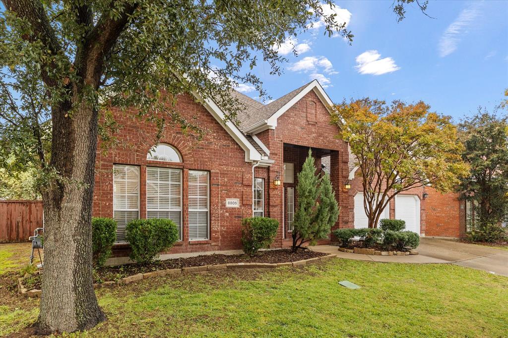 a view of a house with brick walls plants and large tree