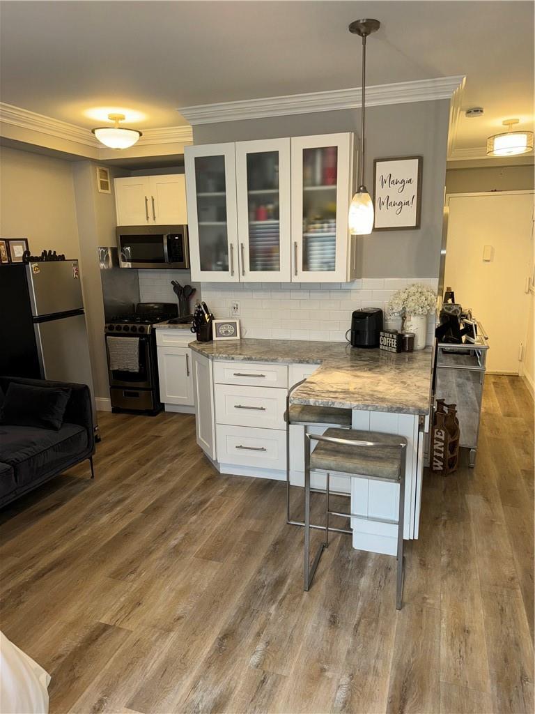 Kitchen with hanging light fixtures, white cabinets, hardwood / wood-style floors, light stone counters, and stove