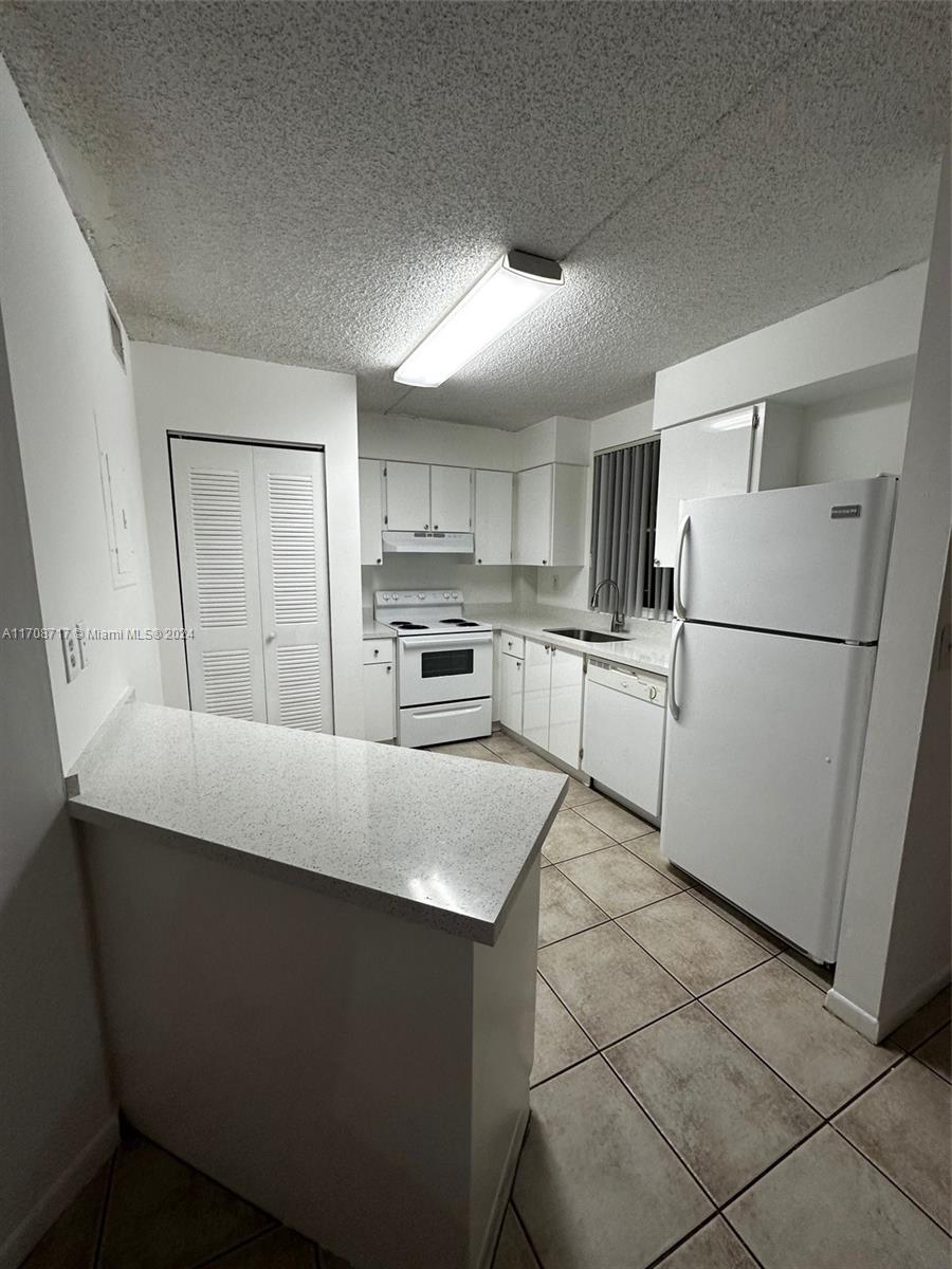 a kitchen with granite countertop a refrigerator a sink and white cabinets