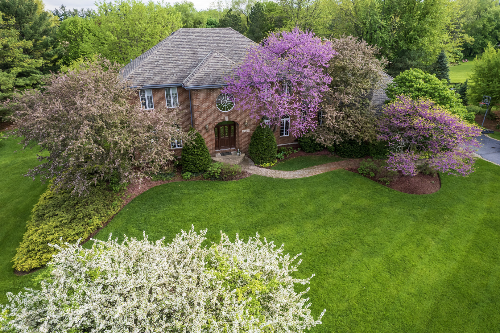 a front view of a house with a yard and fountain in middle of green field