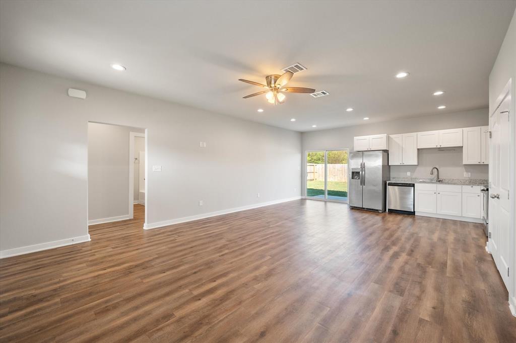 a view of an empty room with wooden floor and a kitchen