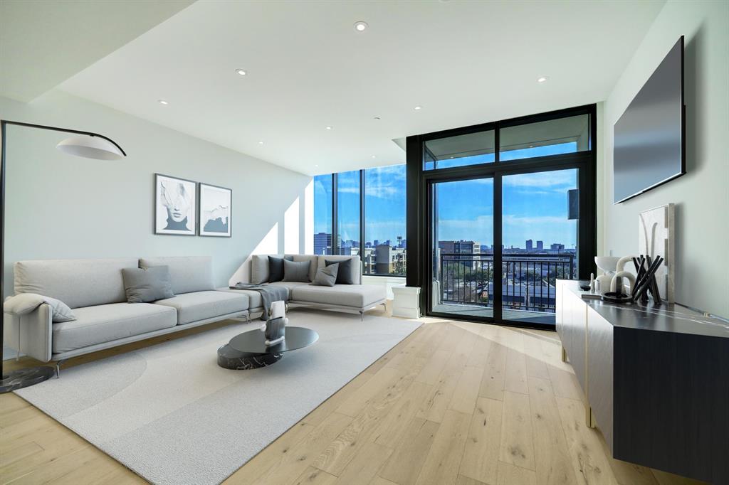 This contemporary living space features an open floor plan with ample natural light, hardwood floors, and a large floor-to-ceiling window that opens to a balcony with an urban view.