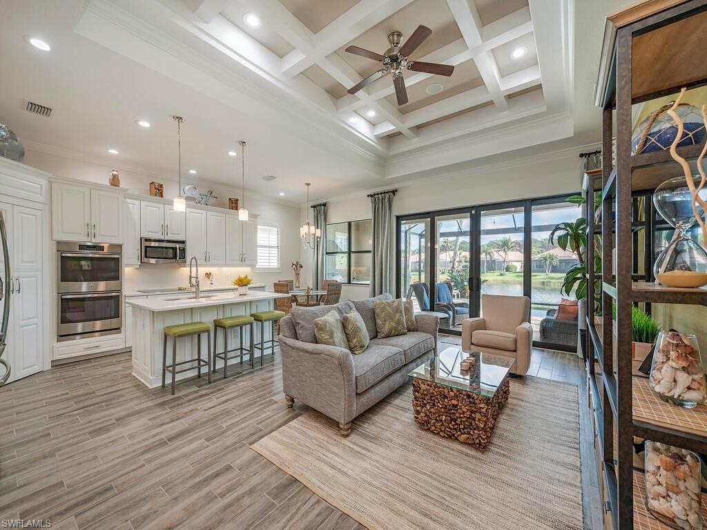 a living room with stainless steel appliances furniture wooden floor and a kitchen view