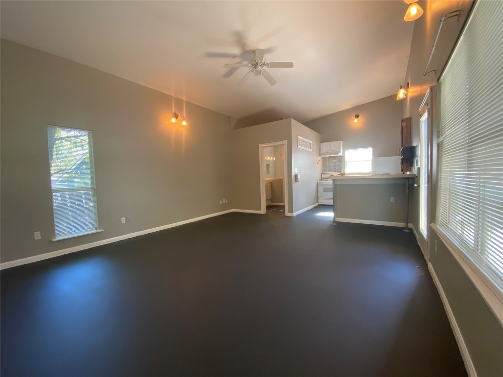 an empty room with wooden floor a kitchen view and windows