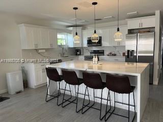 a kitchen with stainless steel appliances granite countertop a sink a stove a refrigerator and white cabinets with wooden floor