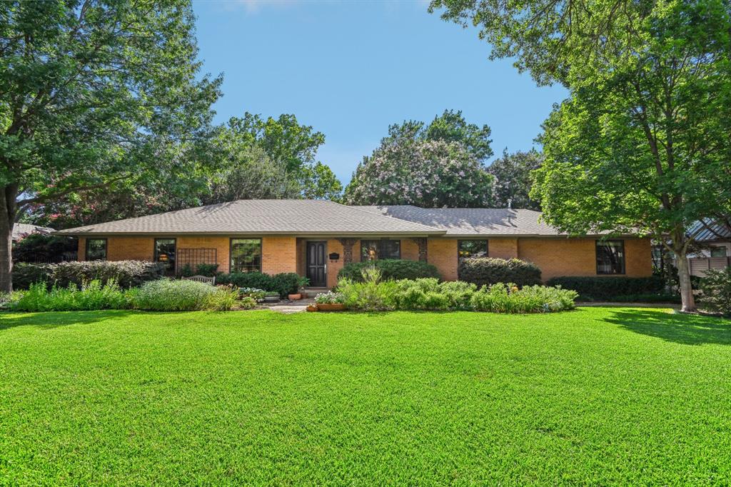 a view of a big house with a big yard and potted plants and large trees