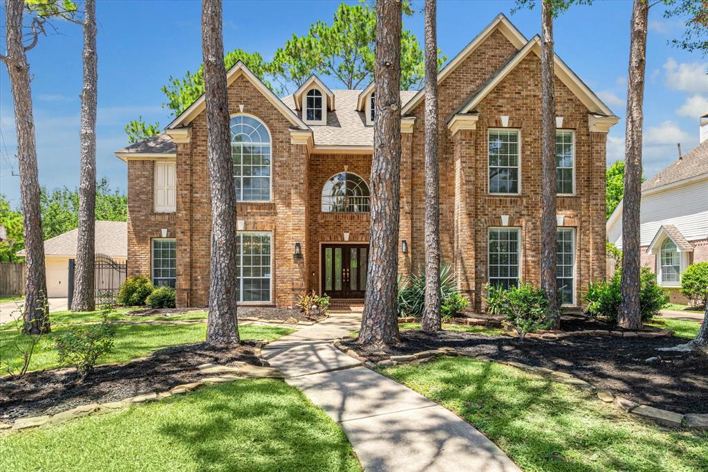 This is a two-story David Weekley brick home featuring tall windows, a stately entrance, and is nestled among mature pine trees, offering a welcoming private home feel.