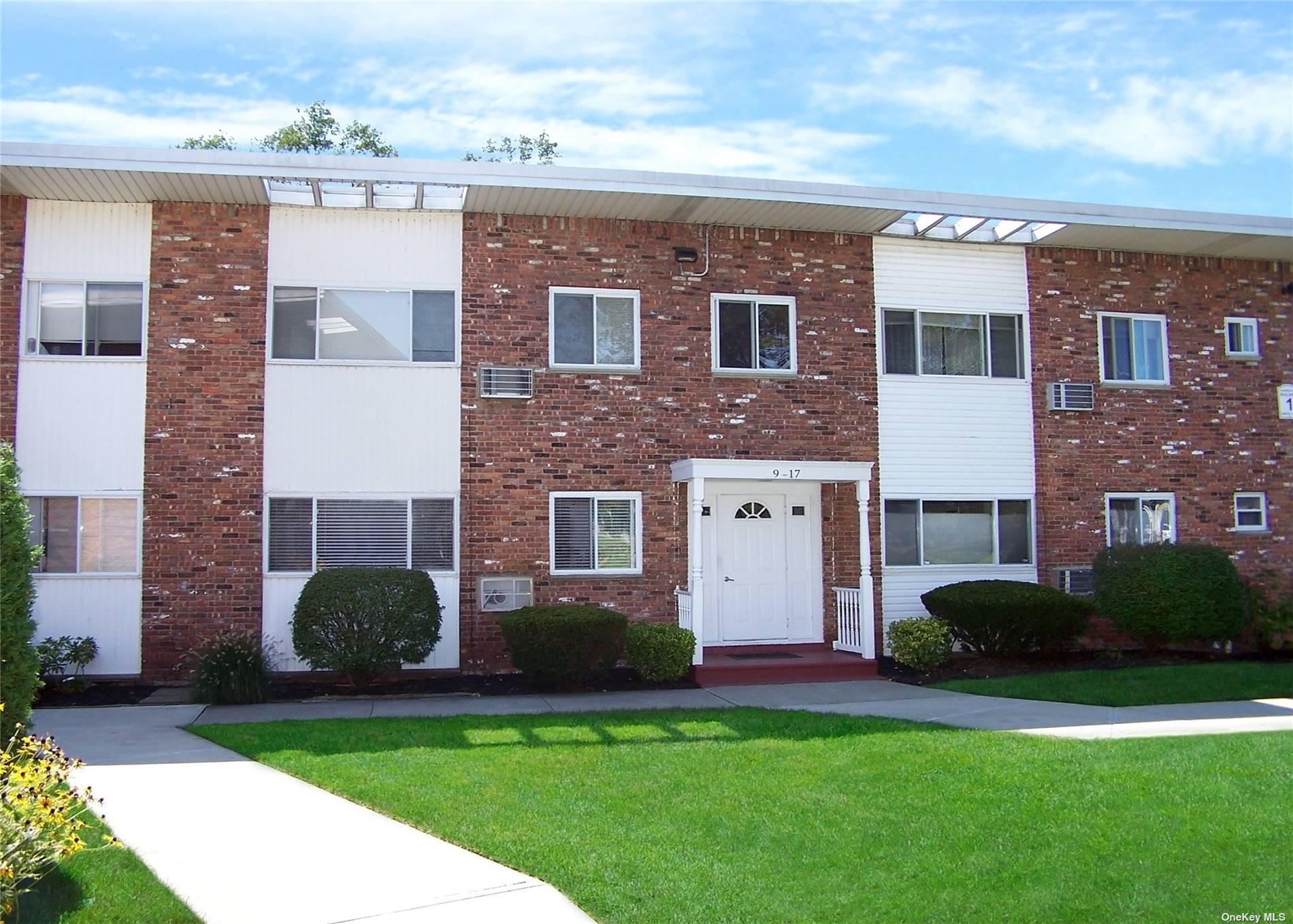 a view of a brick house with a yard plants and a large tree