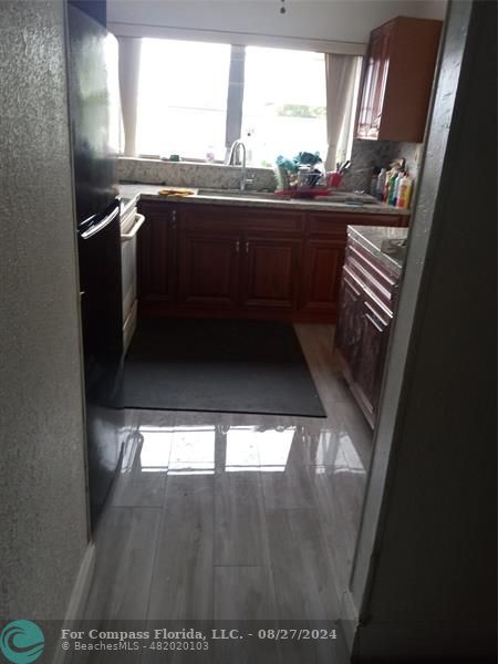 a view of kitchen and an empty room with wooden floor