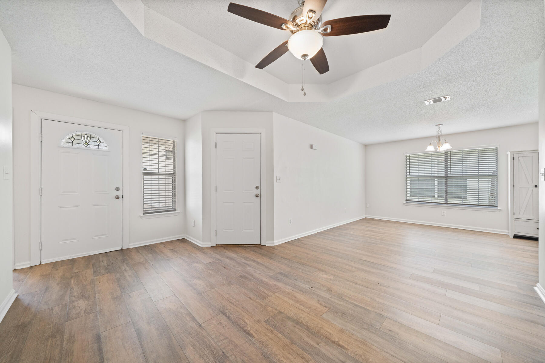 a view of an empty room with wooden floor and a ceiling fan