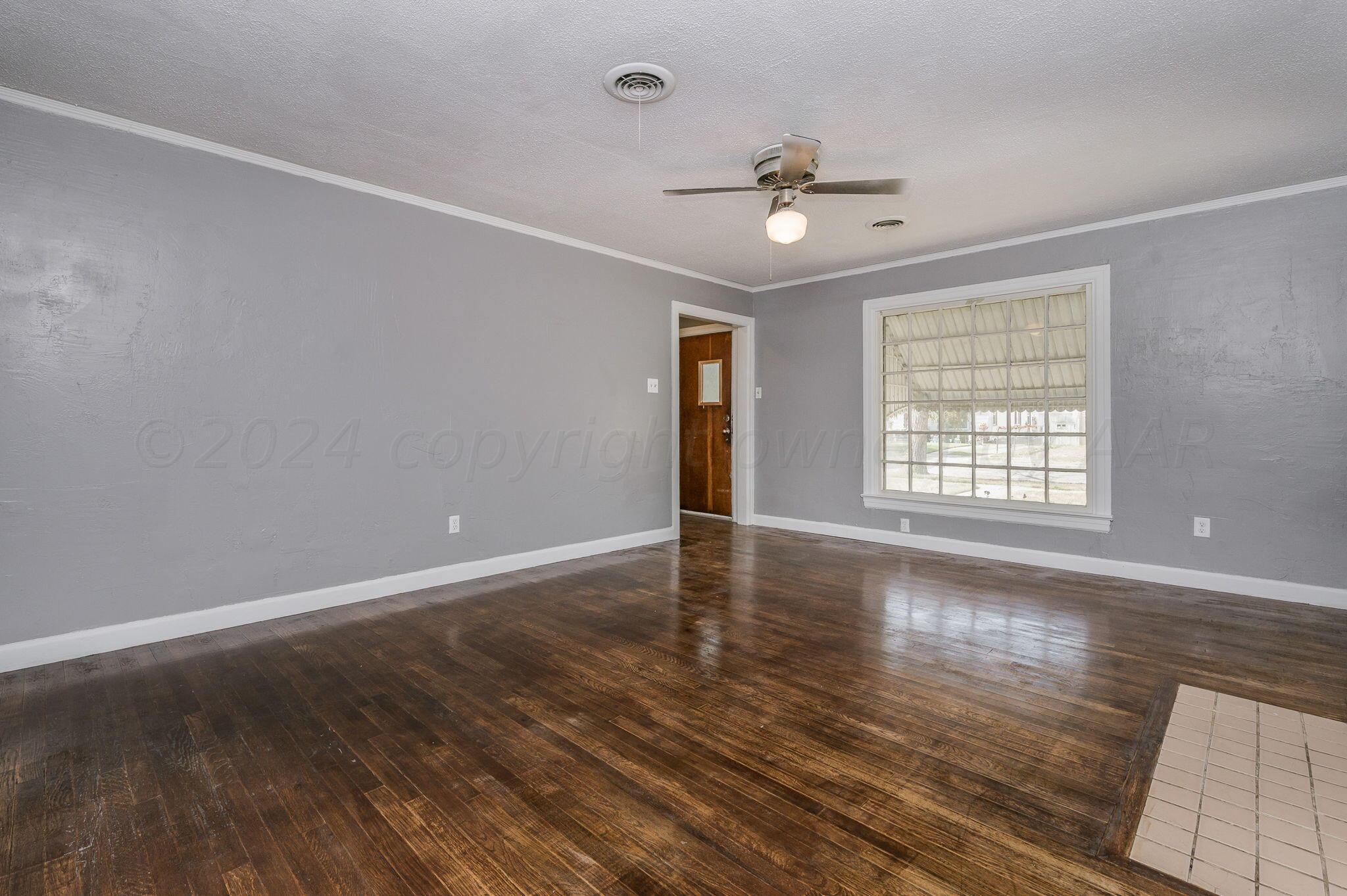 an empty room with wooden floor chandelier fan and windows