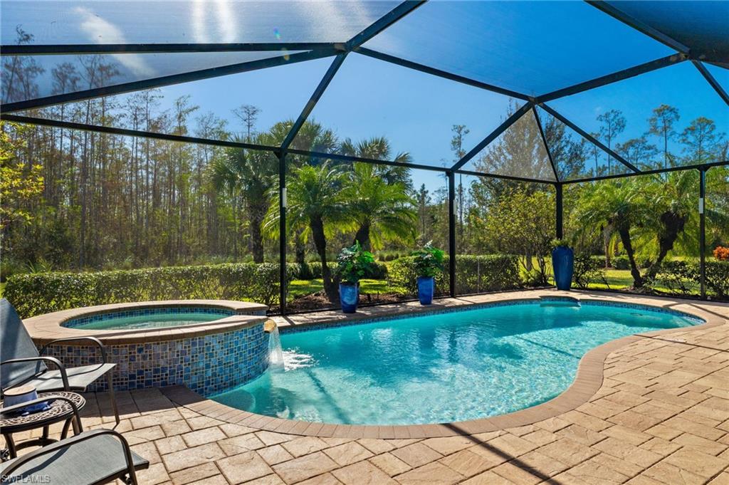 View of pool with glass enclosure, an in ground hot tub, pool water feature, and a patio