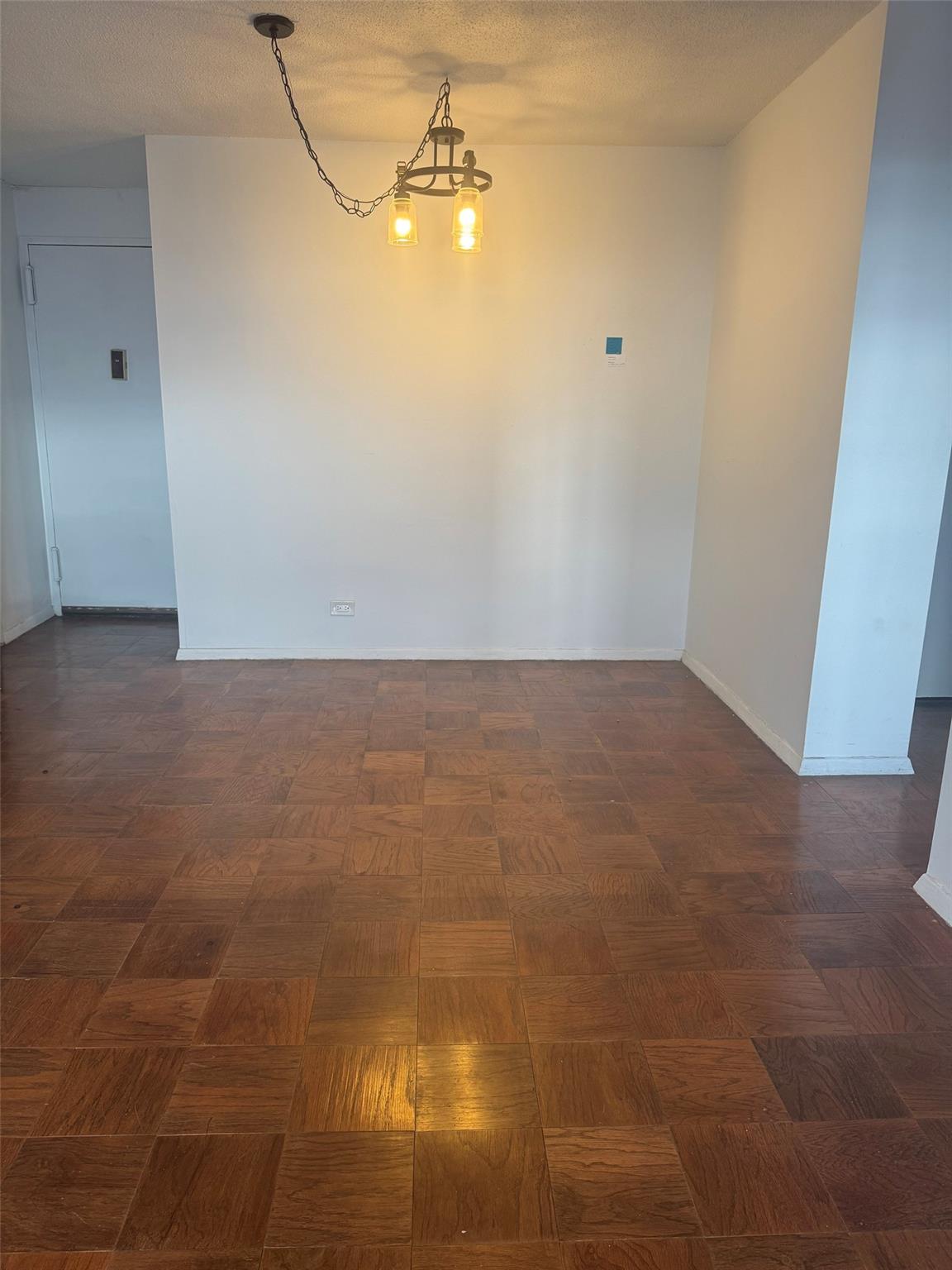 Empty room featuring a notable chandelier, dark parquet floors, and a textured ceiling