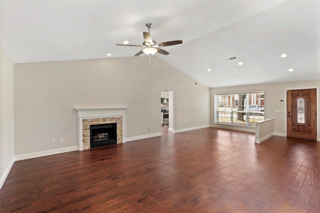 a view of an empty room with wooden floor fireplace and a window