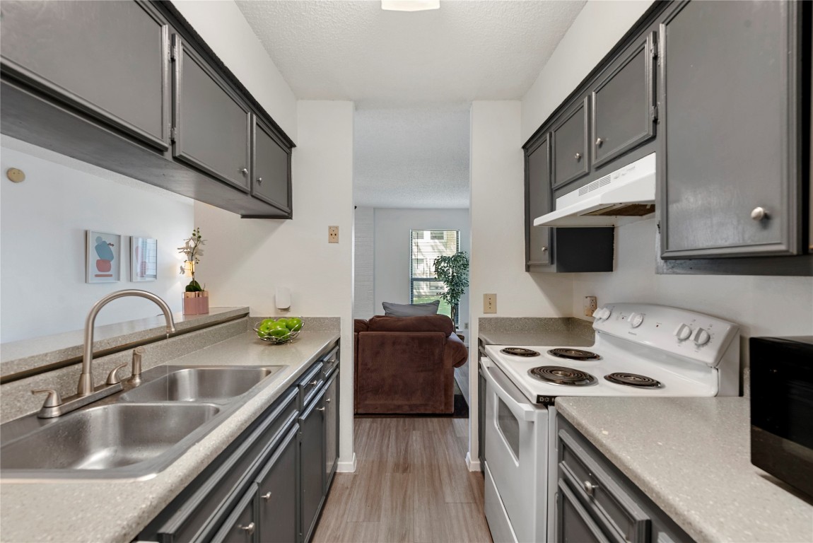 a kitchen with stainless steel appliances a sink a stove and a microwave with wooden floor