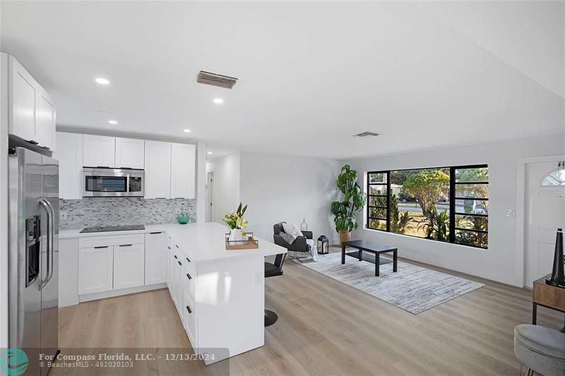 a living room with stainless steel appliances granite countertop furniture wooden floor and a large window